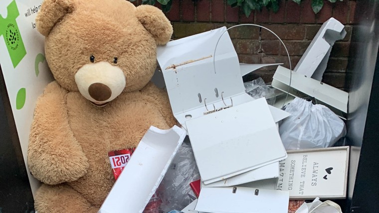 A large teddy bear and other waste items dumped on a floor