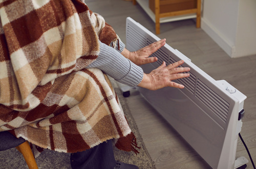 A person with a blanket warming their hands on a radiator at home