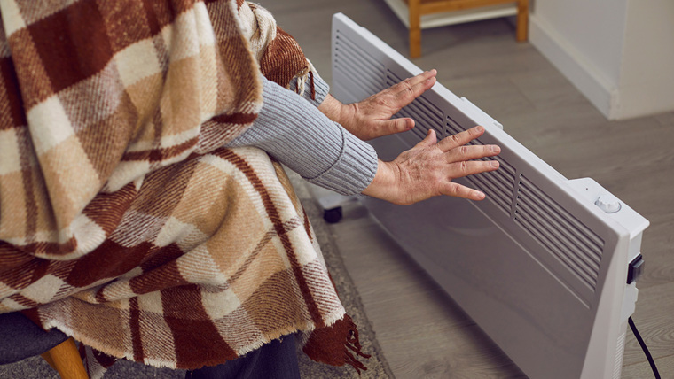 A person with a blanket warming their hands on a radiator at home