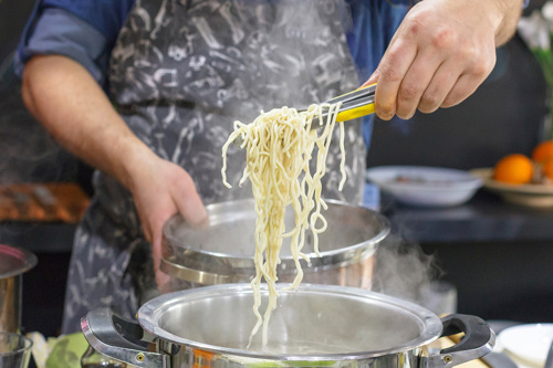 A picture of a person holding a spoonful of cooked spaghetti from a hot pan